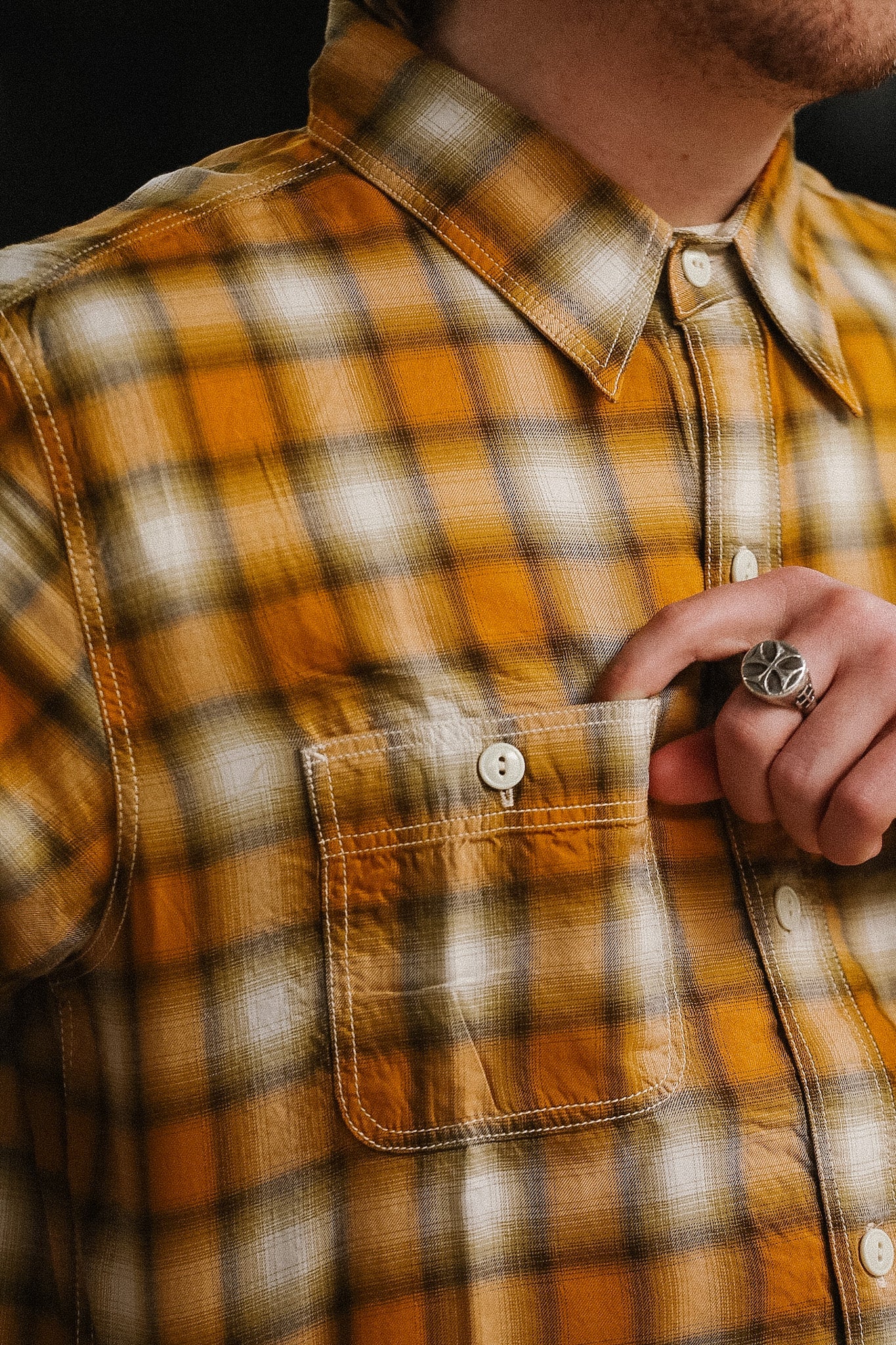 Close-up of a person wearing a yellow and brown plaid shirt with a ring on their finger.