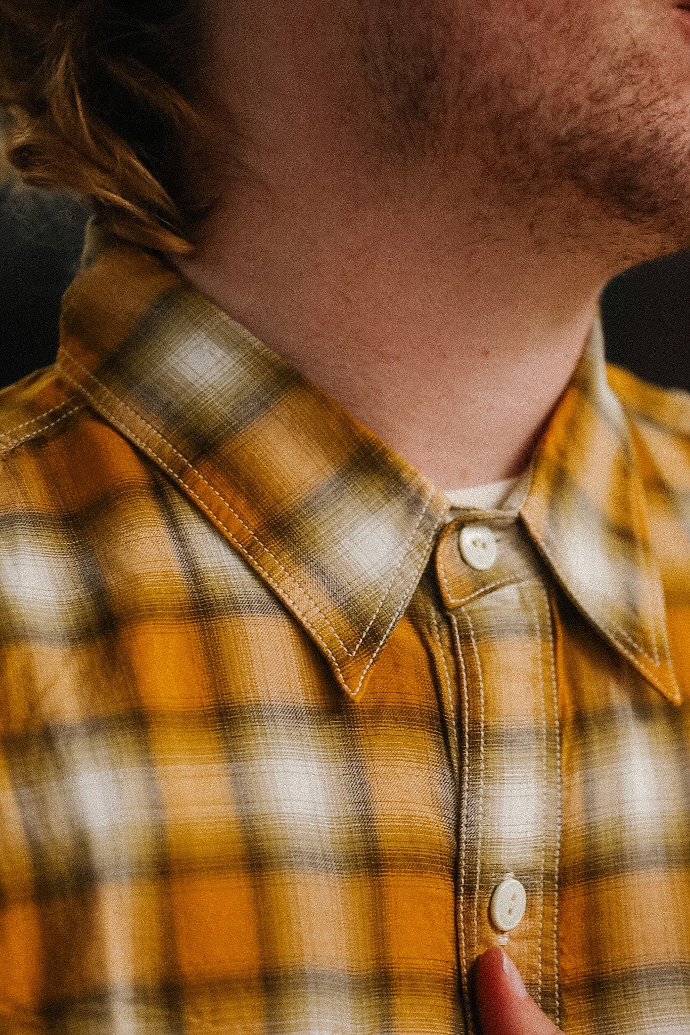 Close-up of a person wearing a plaid shirt with a focus on the collar and buttons.