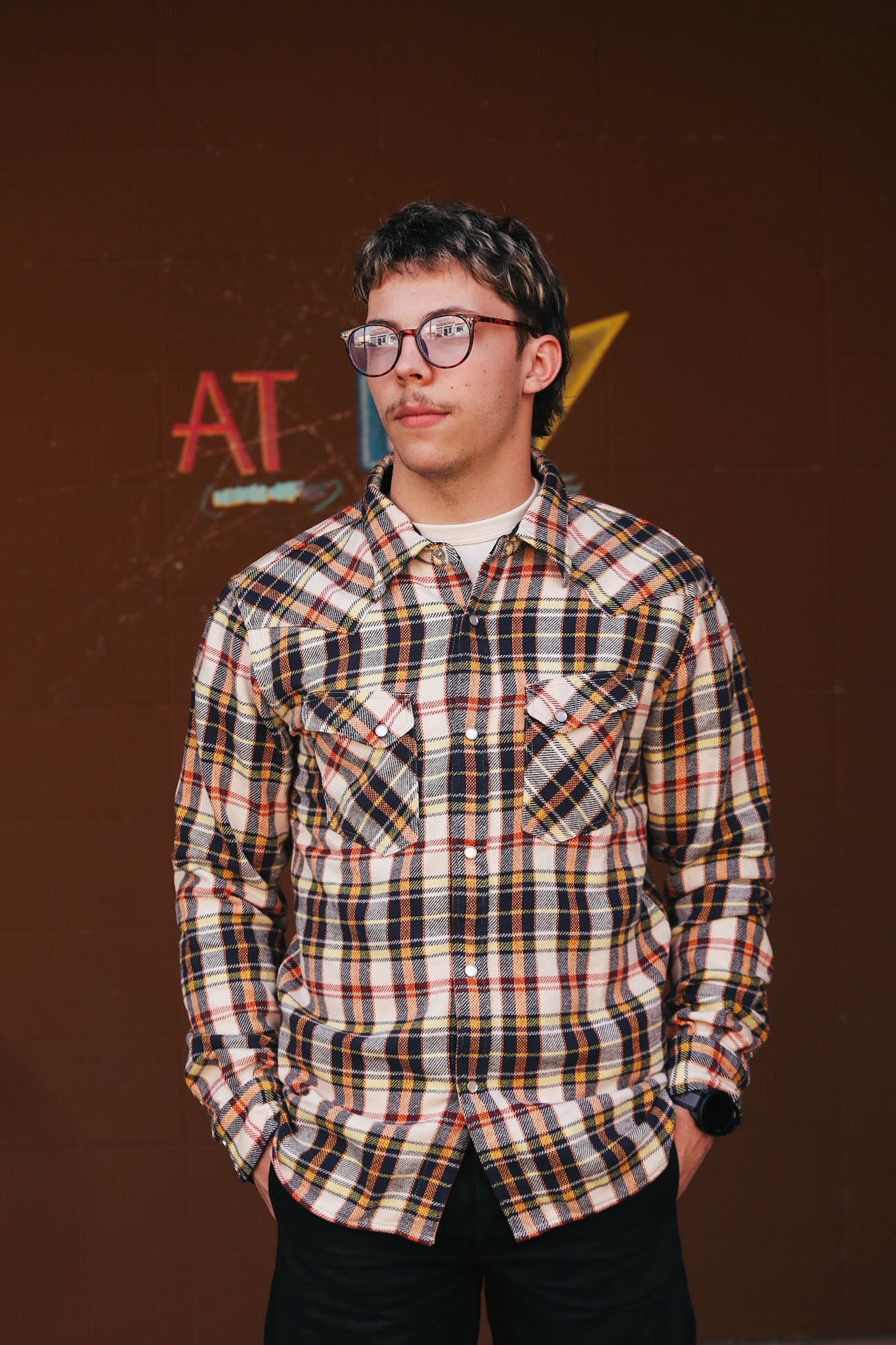 Person wearing a plaid shirt in front of a brown background with logos.