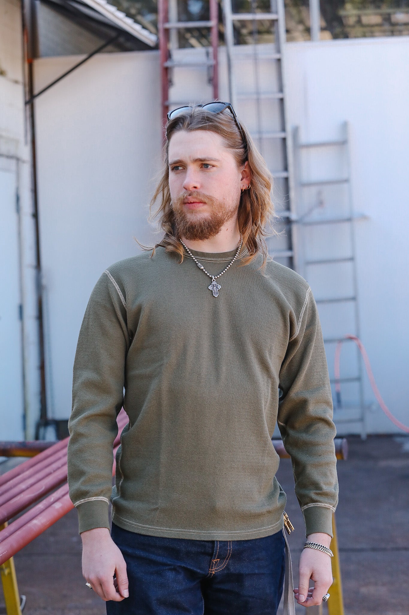Man wearing a green sweater and sunglasses on his head, standing outdoors.