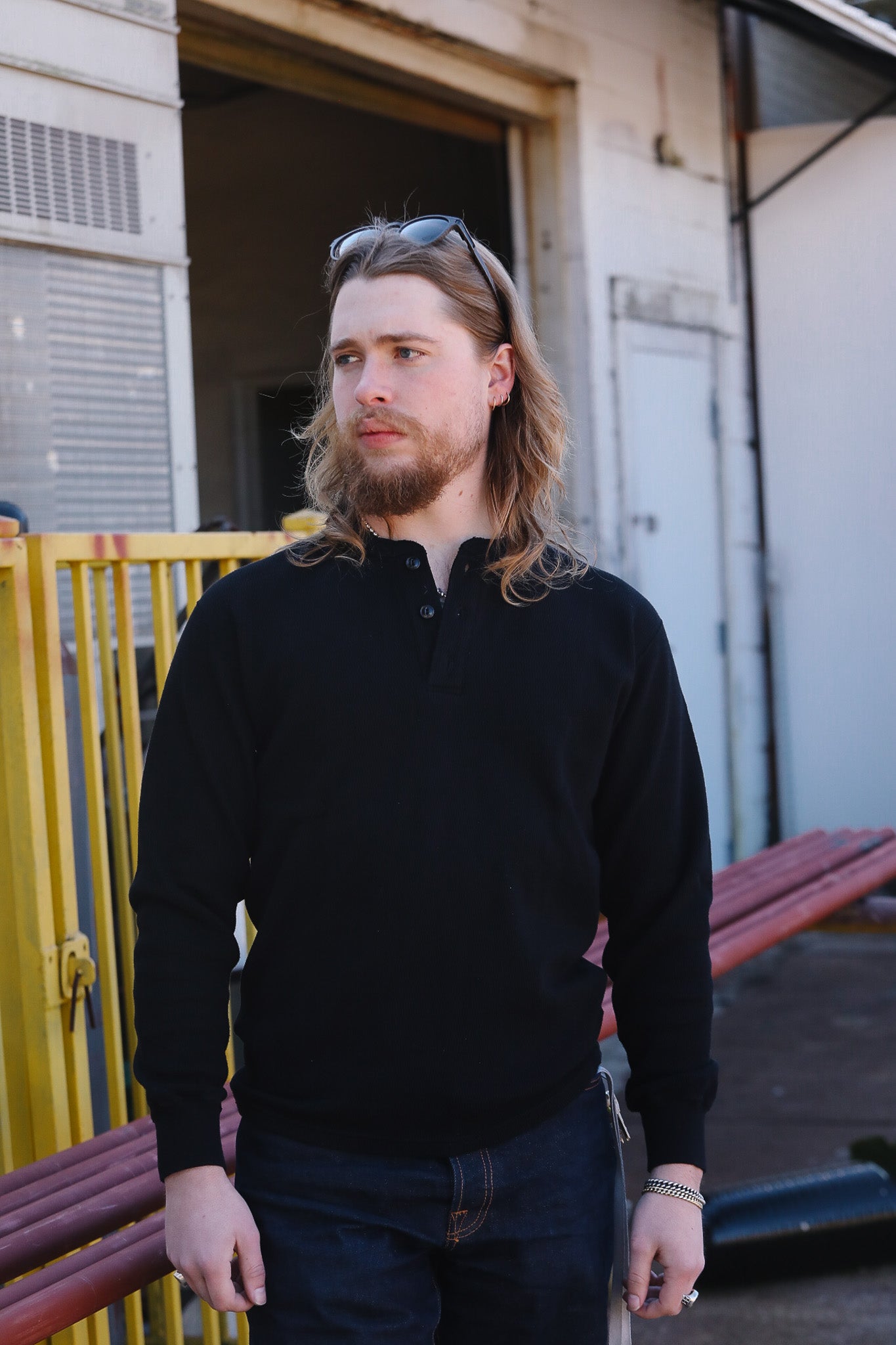Man with long hair and beard wearing a black sweater standing outdoors.