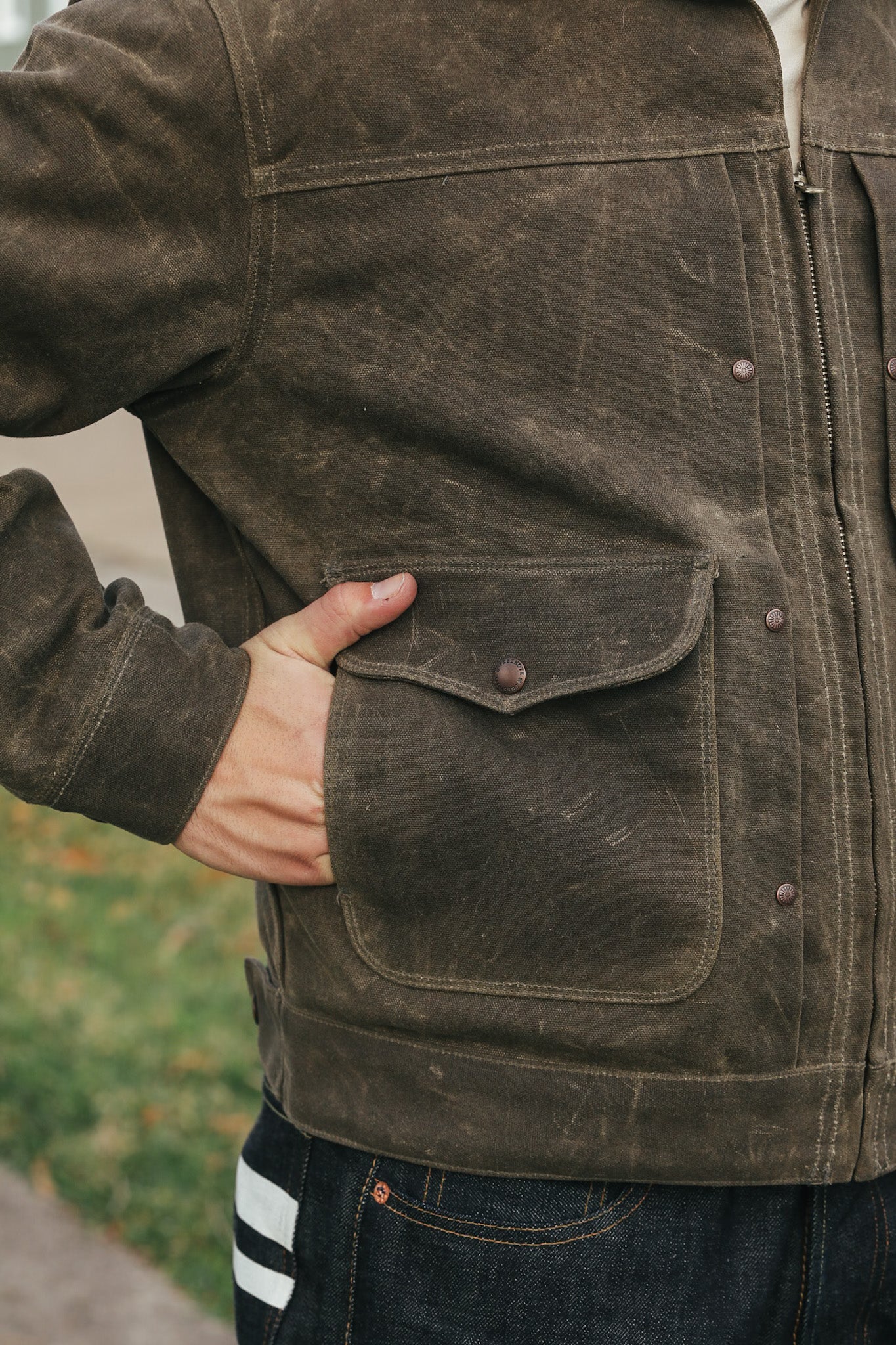 Brown jacket with a pocket and zipper, worn by a person outdoors.