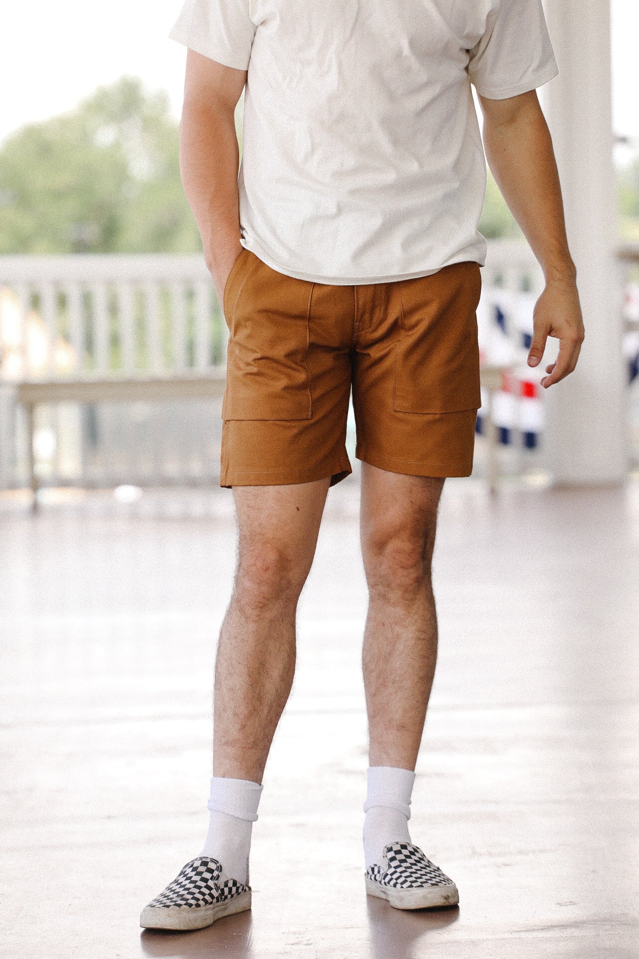 Man wearing camel canvas fatigue shorts with patch pockets, white socks, and checkered slip-on shoes