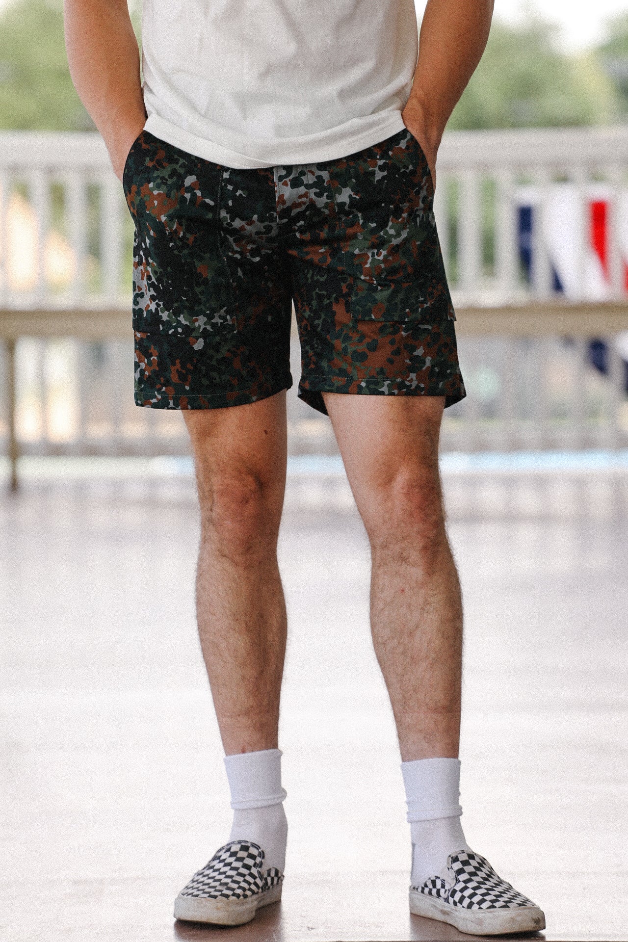 Man wearing diffusion camo fatigue shorts, white socks, and checkered slip-on shoes