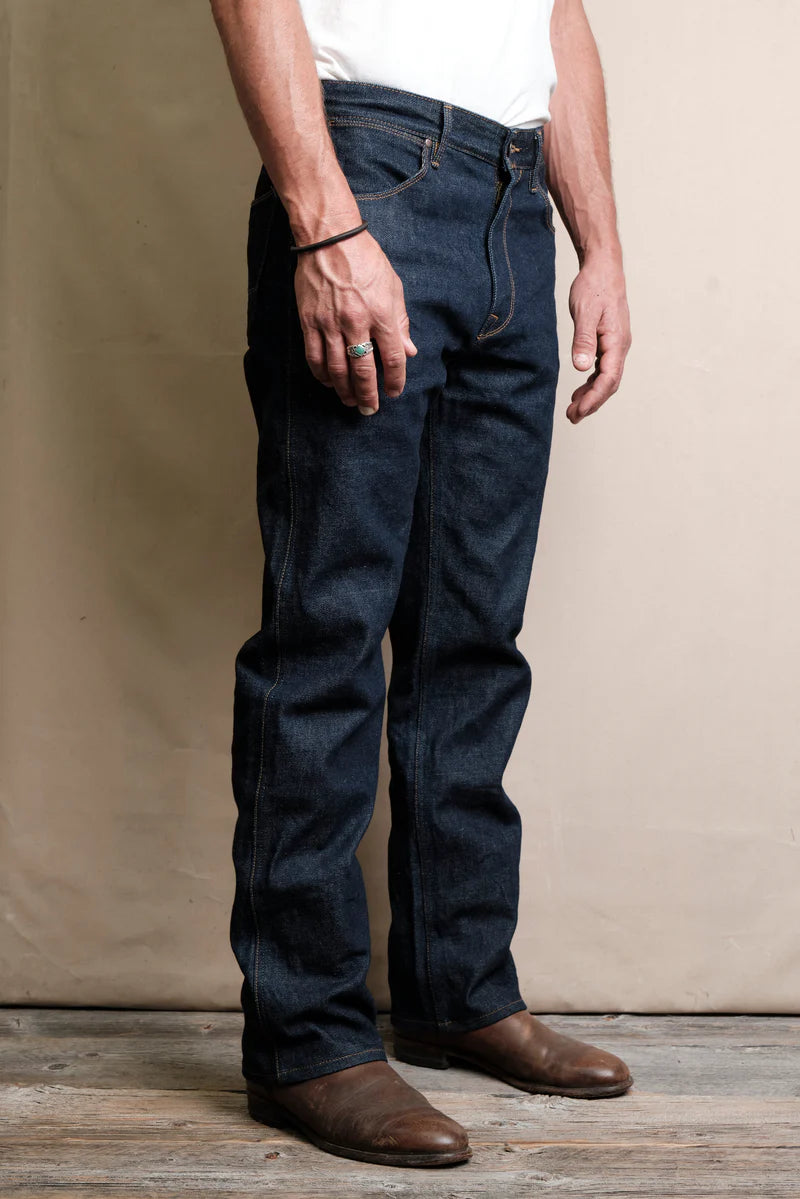 Man wearing straight-leg dark blue denim jeans paired with brown leather boots standing indoors