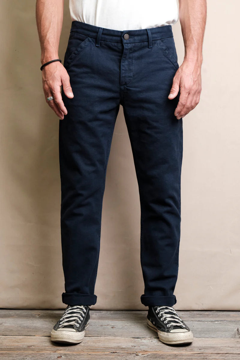 Man wearing dark navy casual pants with rolled cuffs and black sneakers on wooden floor