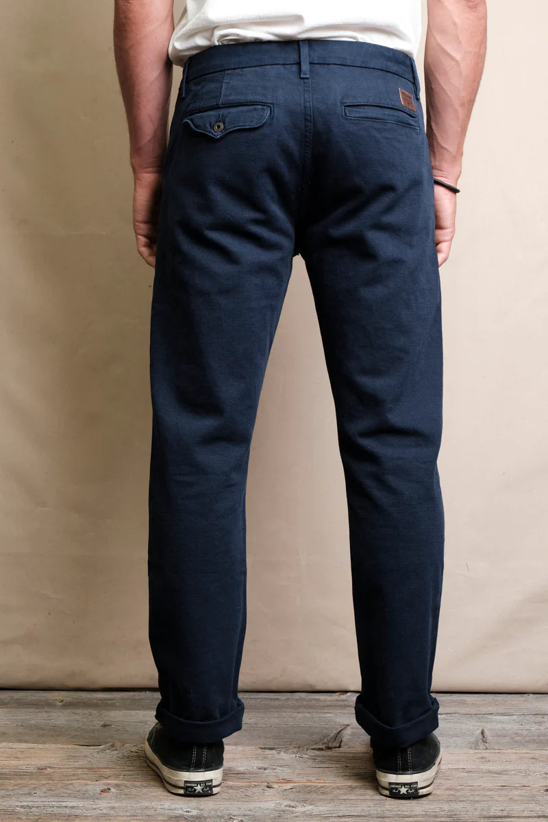 Rear view of man wearing navy blue casual pants with cuffed hems and black sneakers on wooden floor