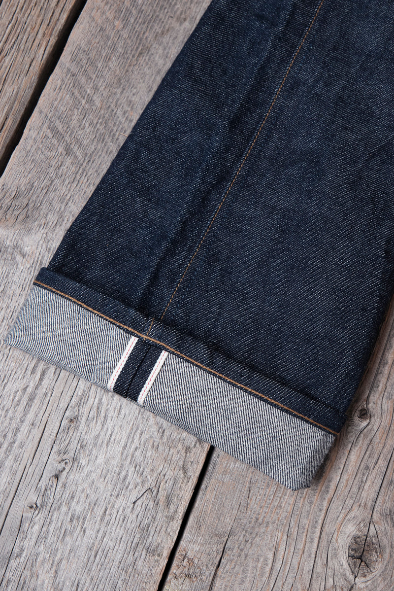 Close-up of dark blue selvedge denim jeans cuff with orange stitching on a rustic wooden surface