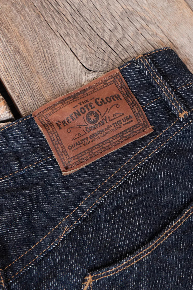 Close-up of Freenote Cloth leather label on dark blue denim jeans with orange stitching on wooden surface