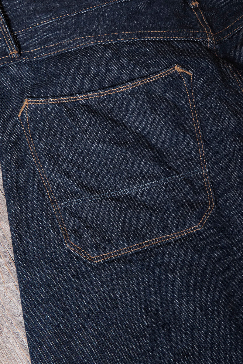 close-up of dark blue denim jeans back pocket with orange stitching on wooden surface