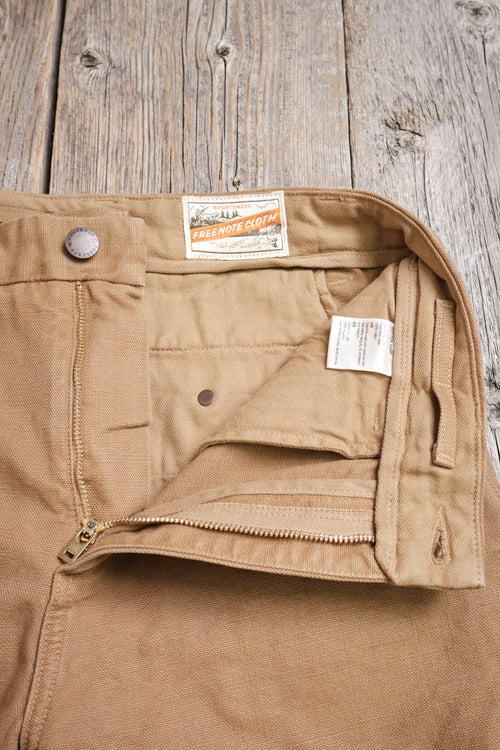 Close-up of beige Freenote Cloth work pants with zipper and button detail on wooden surface