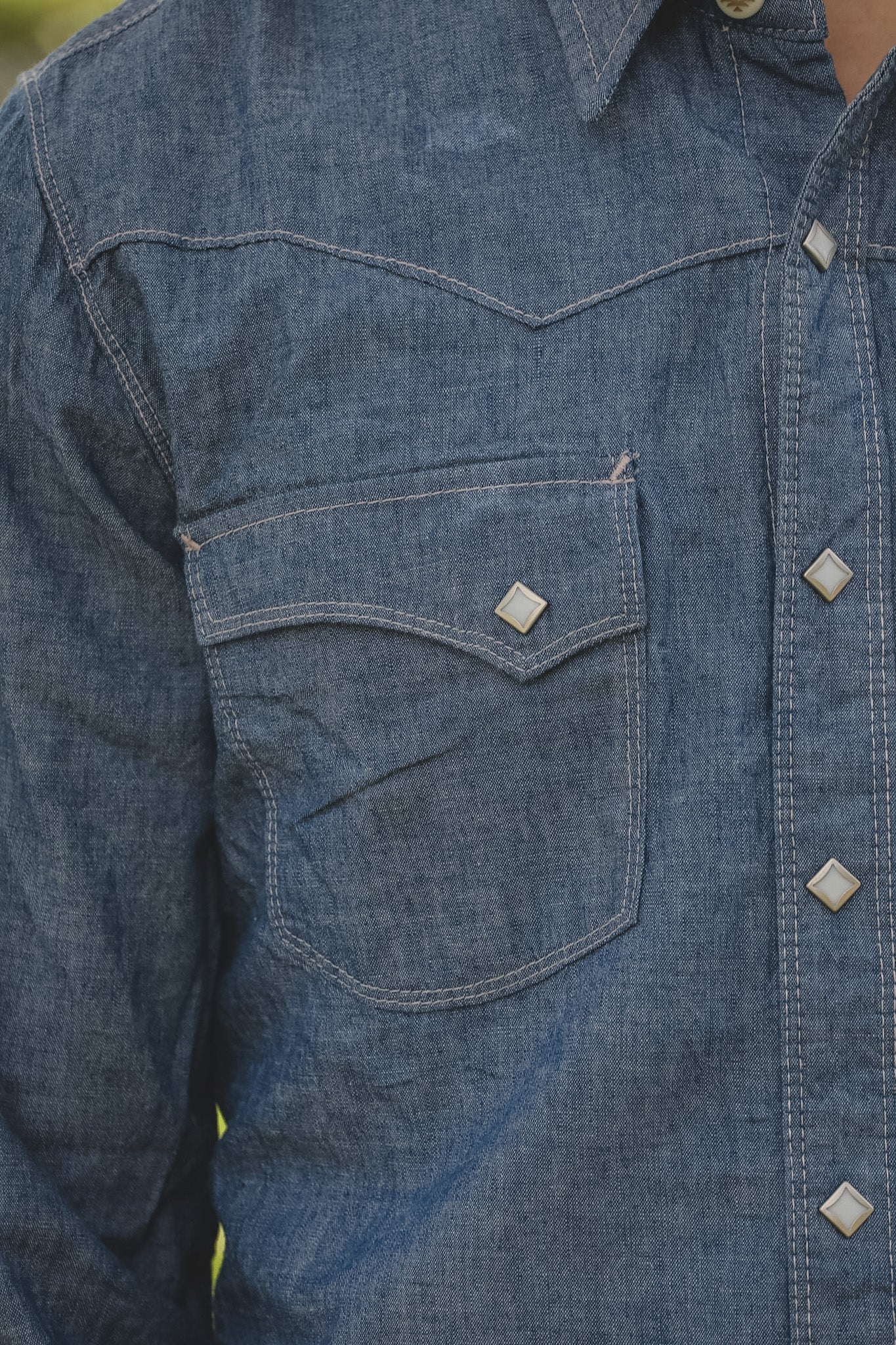 Close-up of a blue denim shirt with a pocket and buttons.