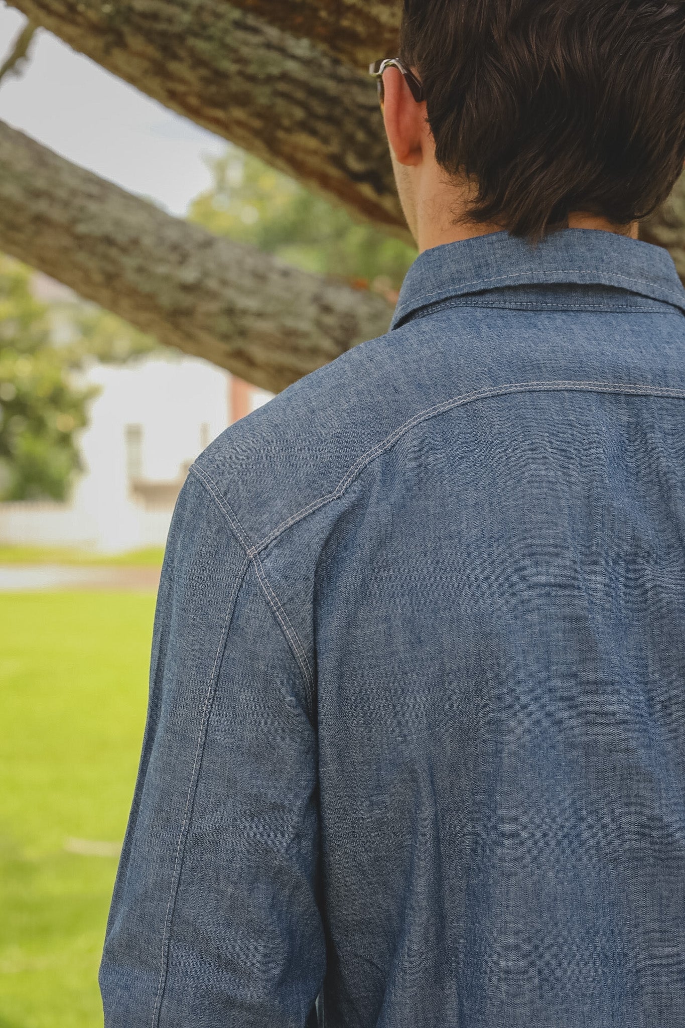Person wearing a blue denim jacket standing outdoors with a tree in the background