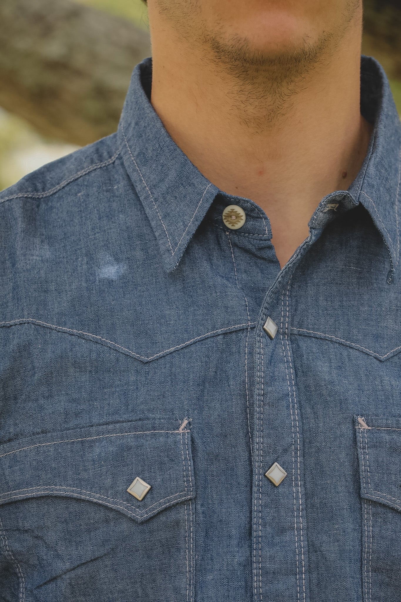 Close-up of a person wearing a blue denim shirt with a blurred background