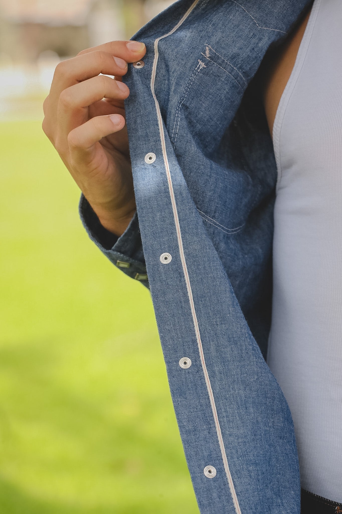Close-up of a person wearing a blue denim shirt with a blurred green background