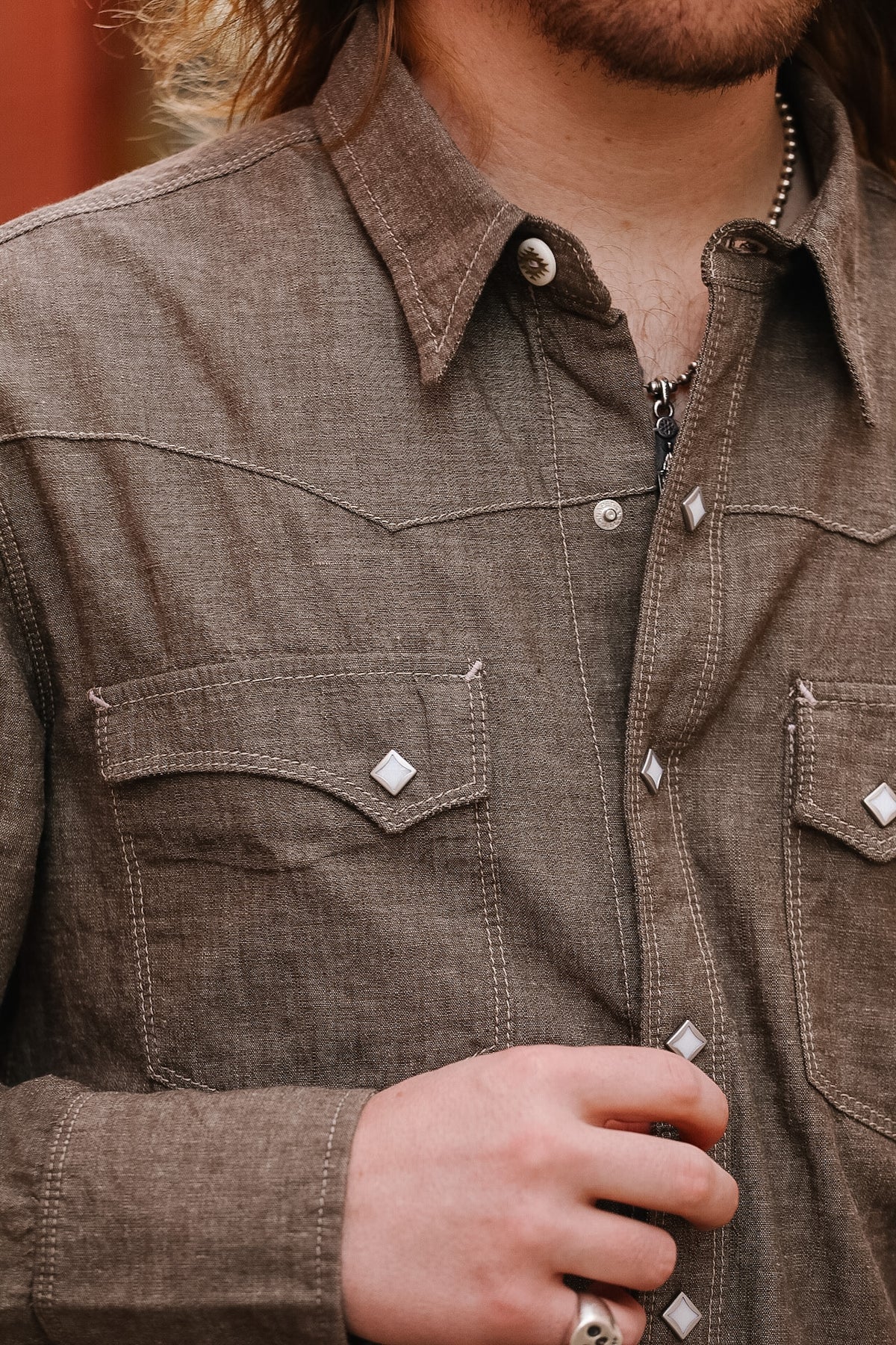 Close-up of a person wearing a brown denim shirt with visible buttons and a pocket.