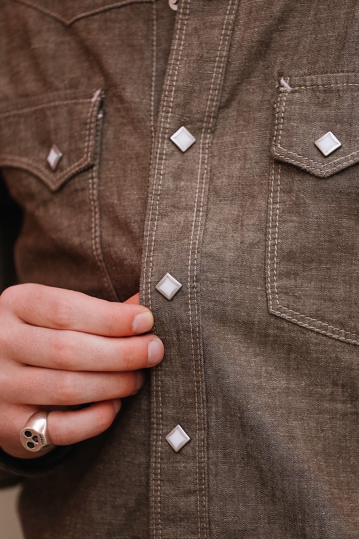 Close-up of a brown denim jacket with buttons and a hand adjusting it.