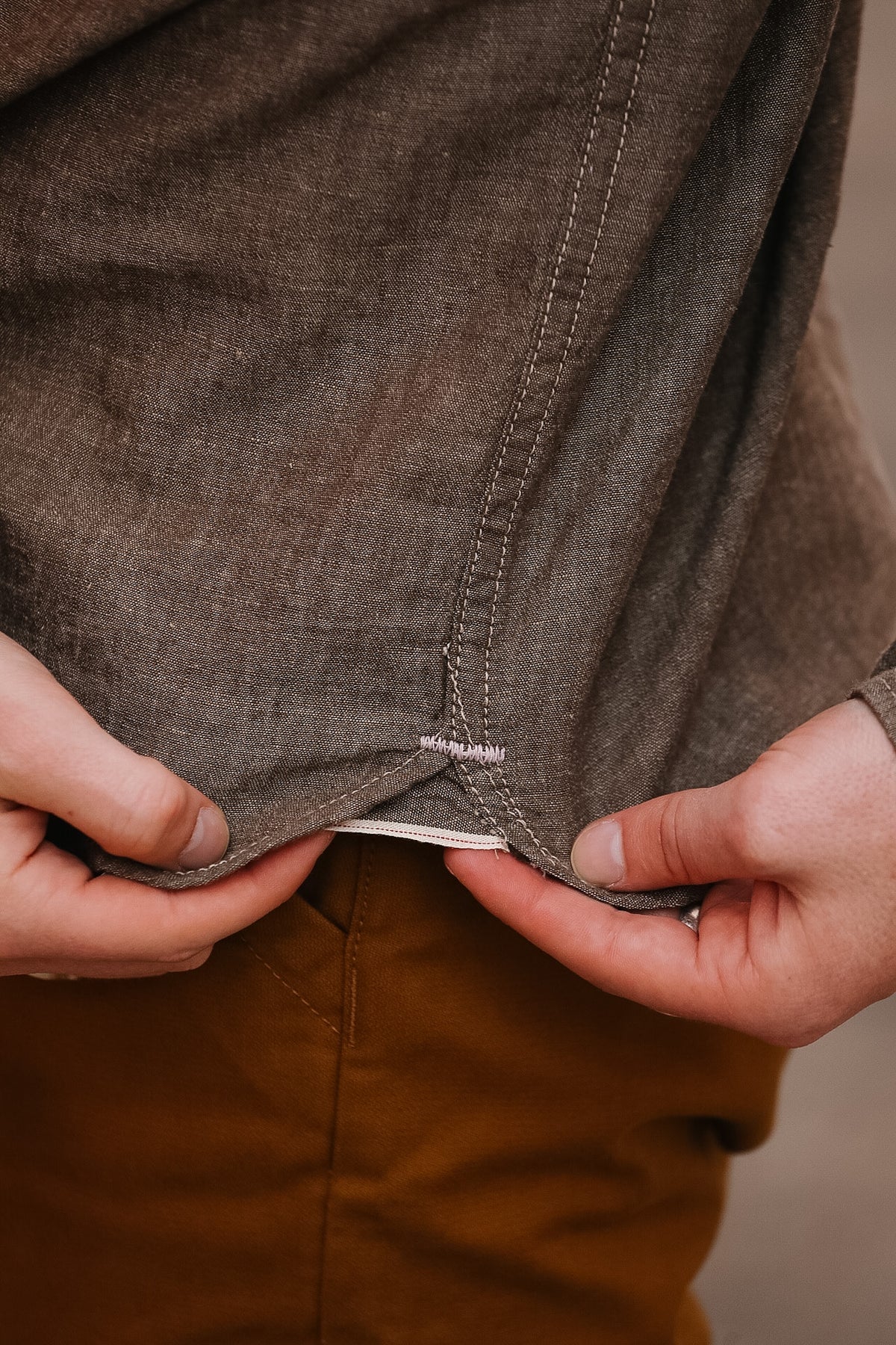 Close-up of a person adjusting the waistband of brown pants.