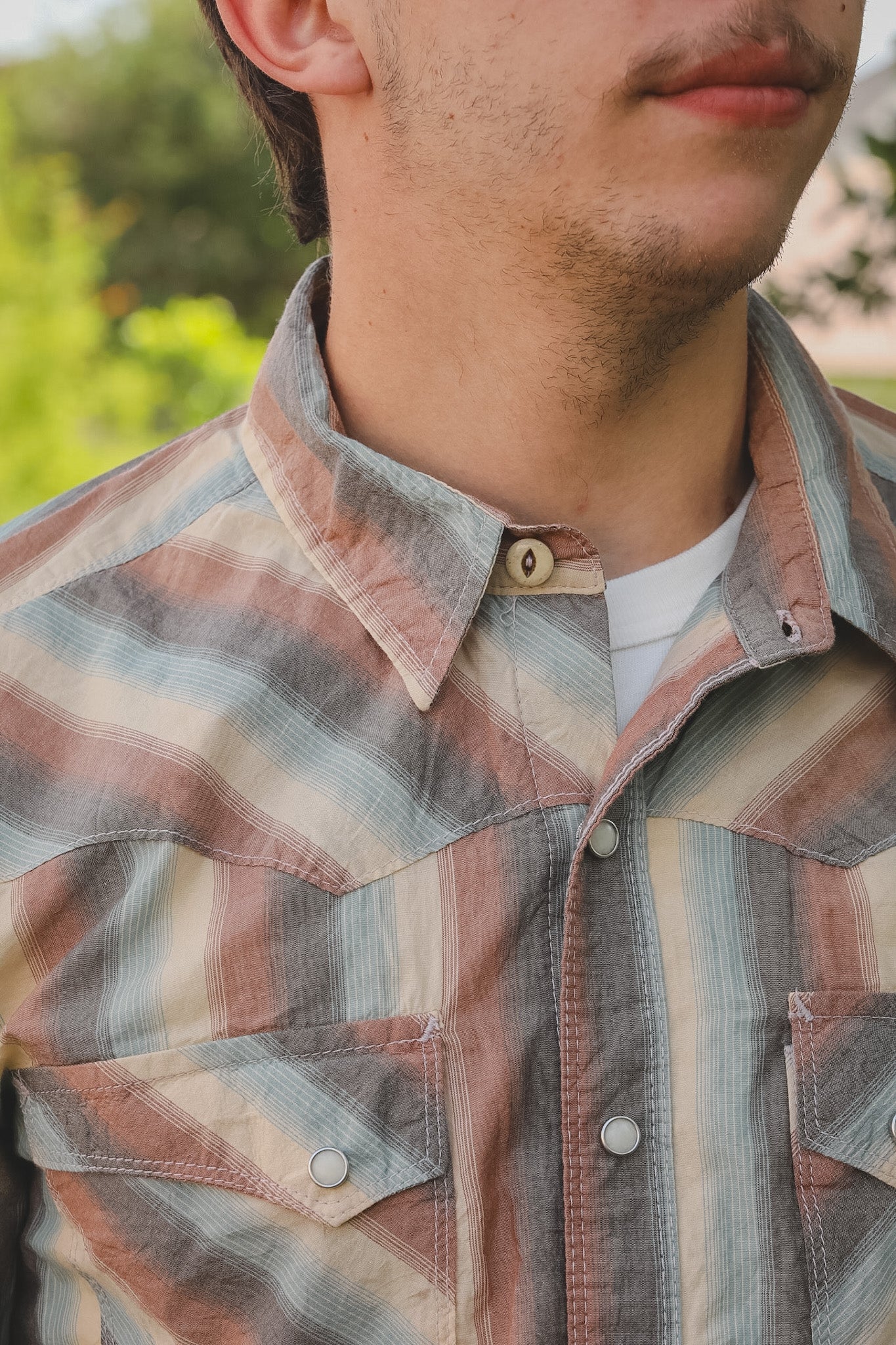 Close-up of a person wearing a plaid shirt with a blurred natural background