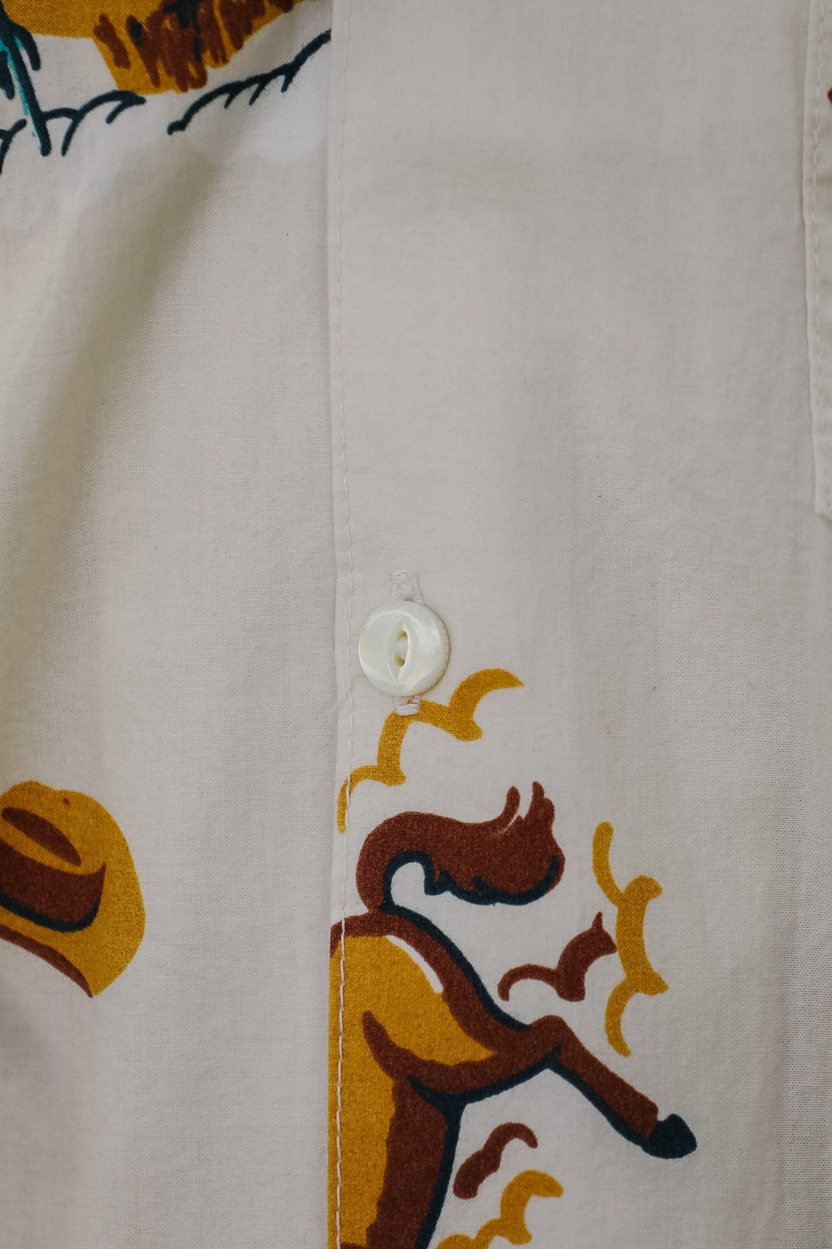 Close-up of a white button-up shirt featuring a colorful printed graphic of a cowboy riding a horse, with a yellow hat and dark blue decorative elements.