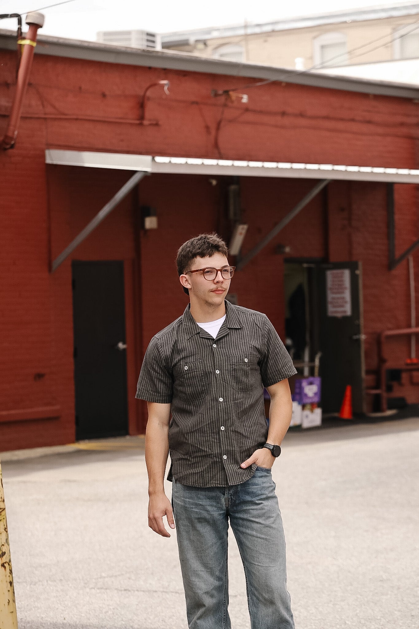 Man standing in front of a red brick building wearing a patterned shirt and jeans.