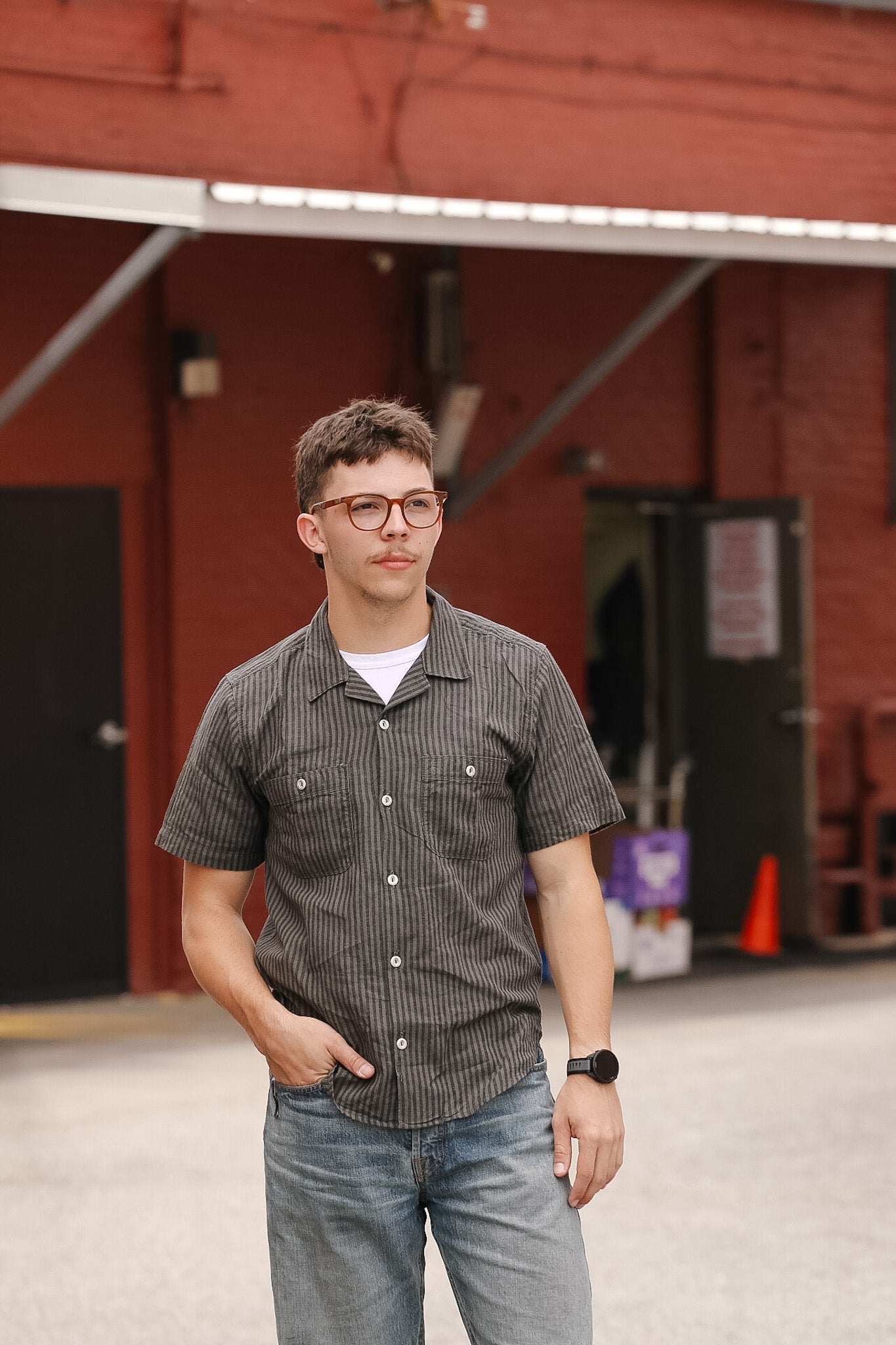 Man wearing a checkered shirt and jeans standing in front of a red building.