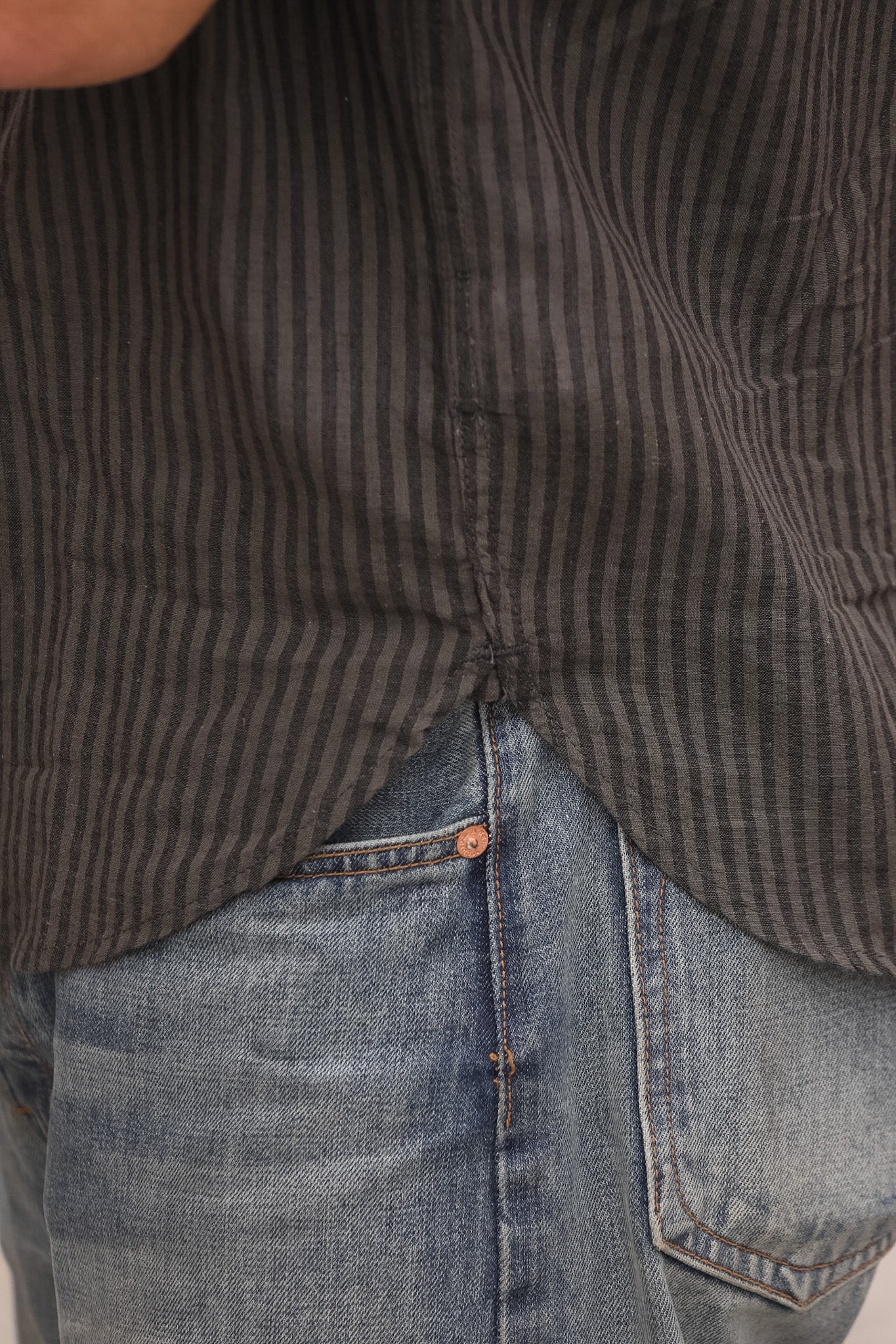 Close-up of a person wearing a brown striped shirt and blue jeans.