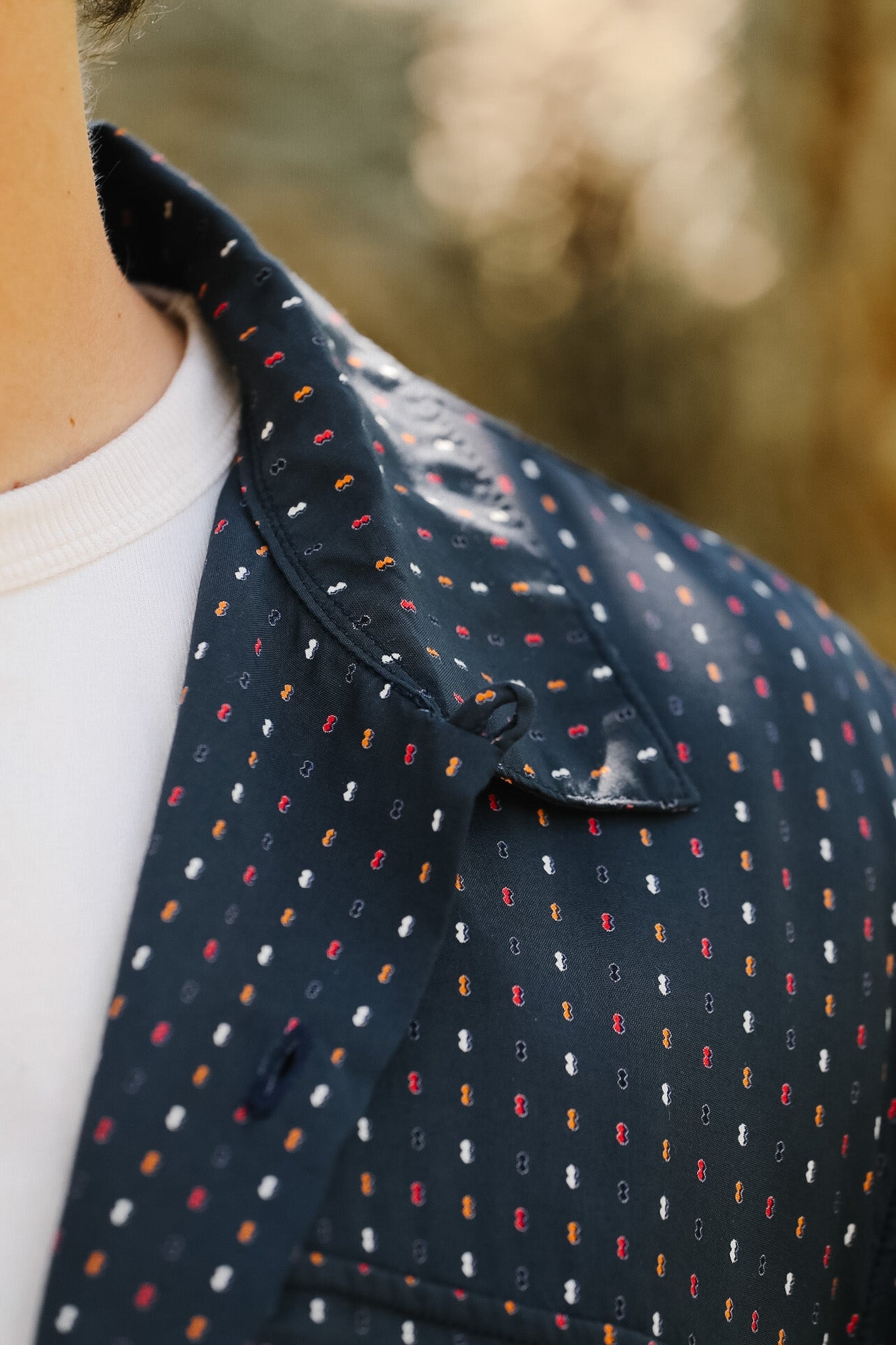 Close-up of a person wearing a navy blue shirt with a subtle pattern, blurred natural background