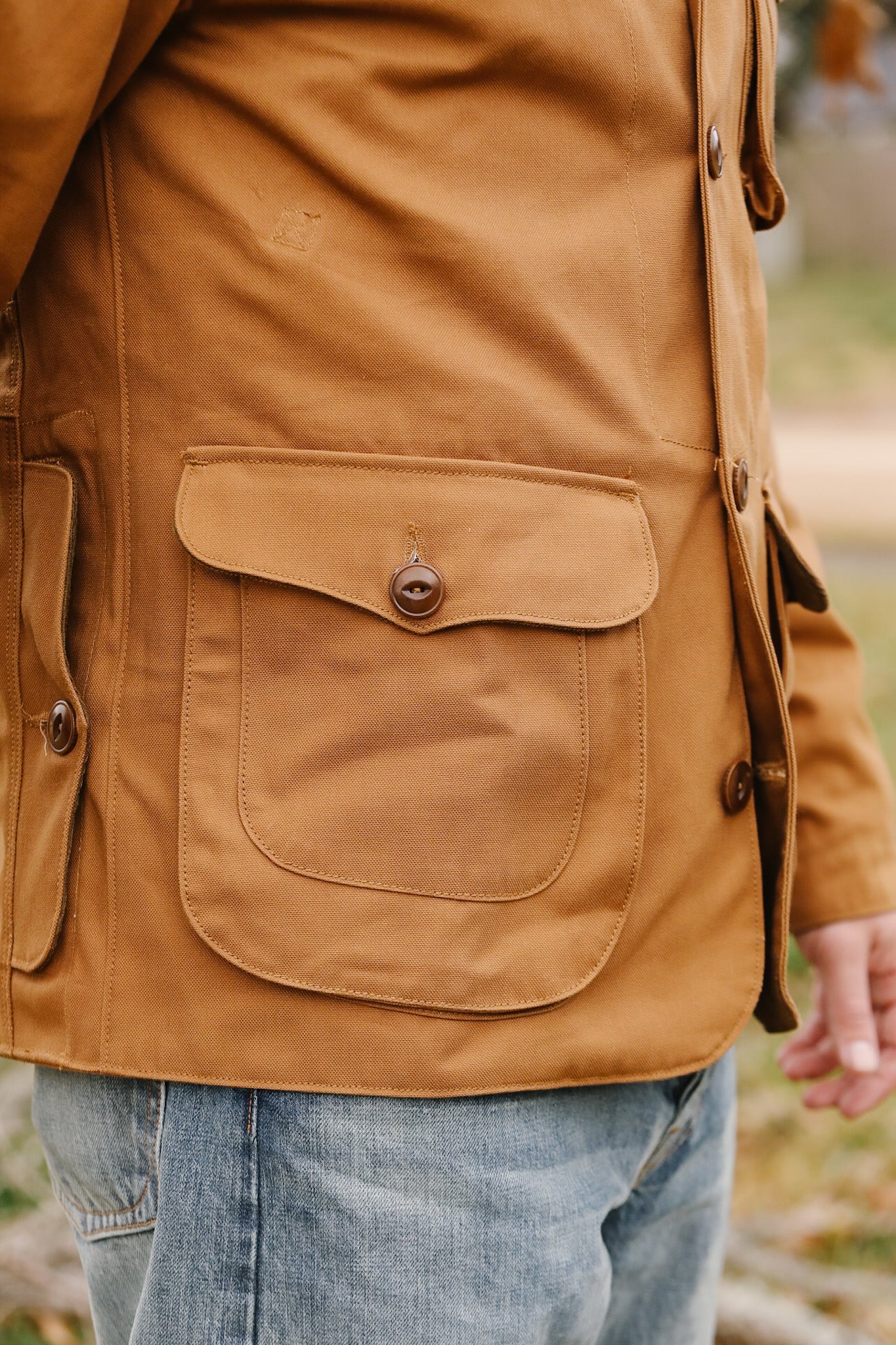 Close-up of a brown jacket with a pocket and button, blurred background