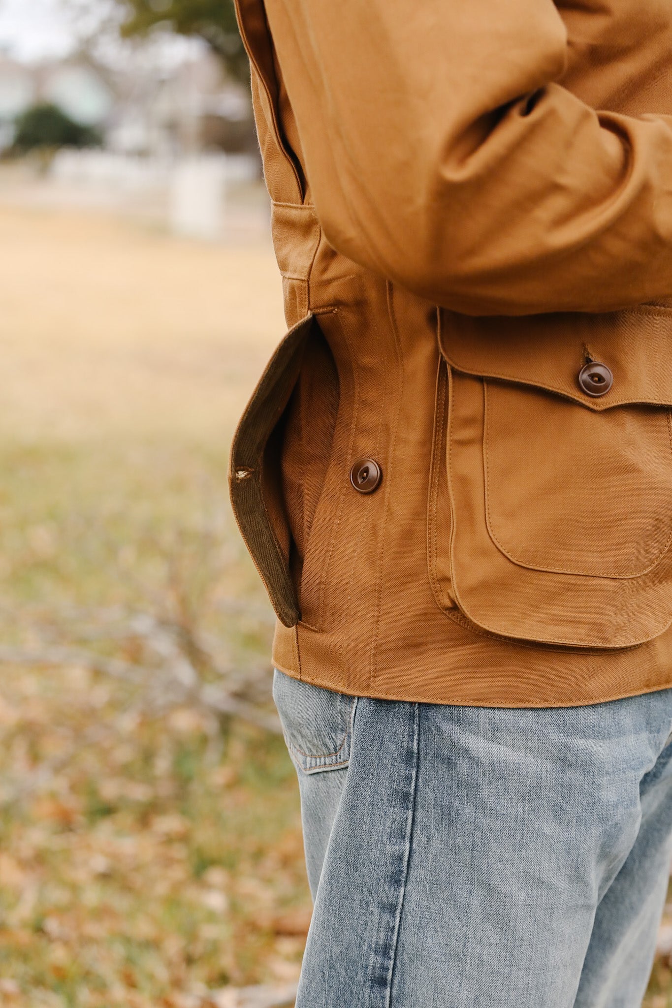 Person wearing a brown jacket with a blurred outdoor background