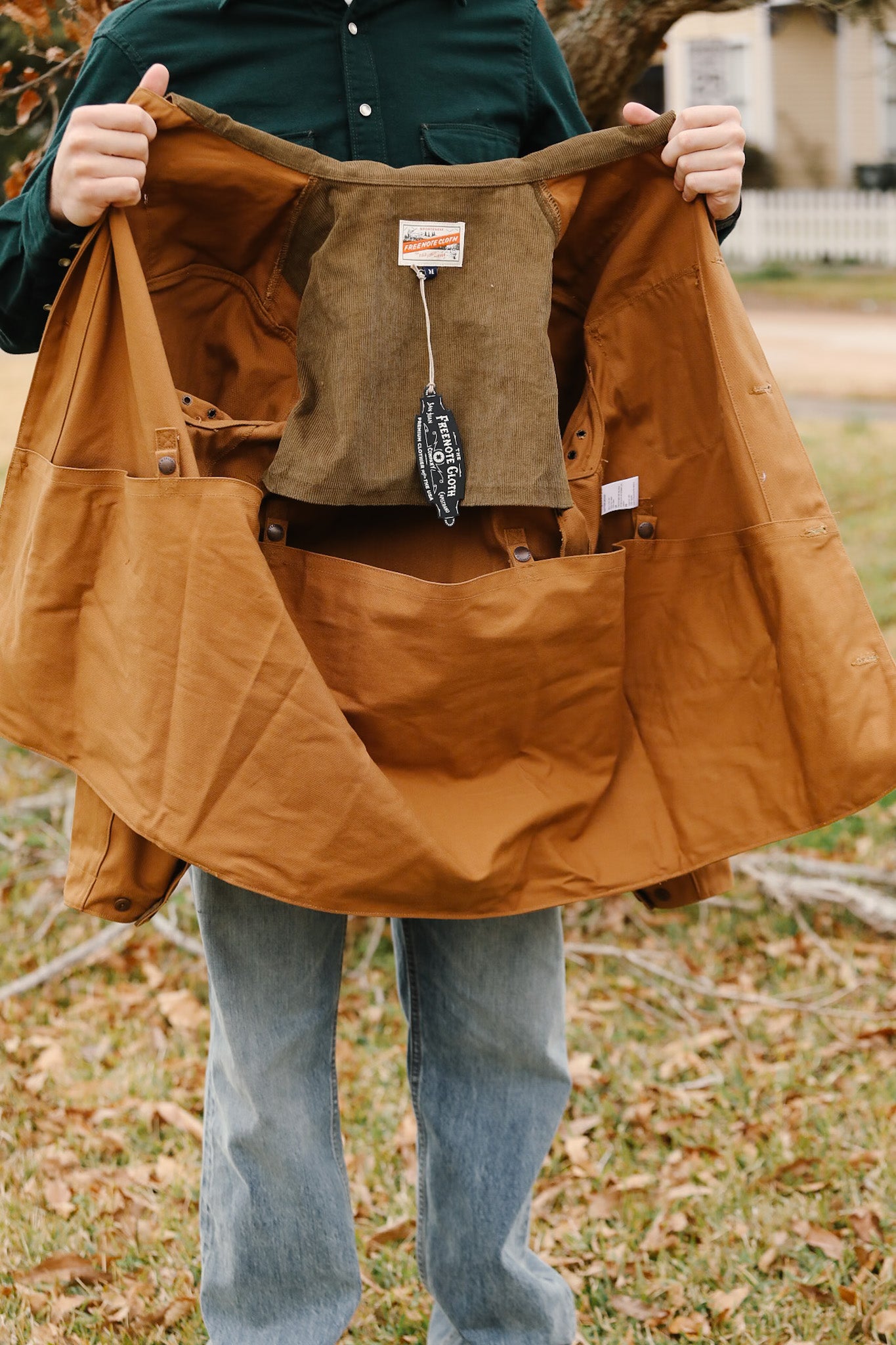 Person holding a brown leather apron with a visible brand label outdoors.