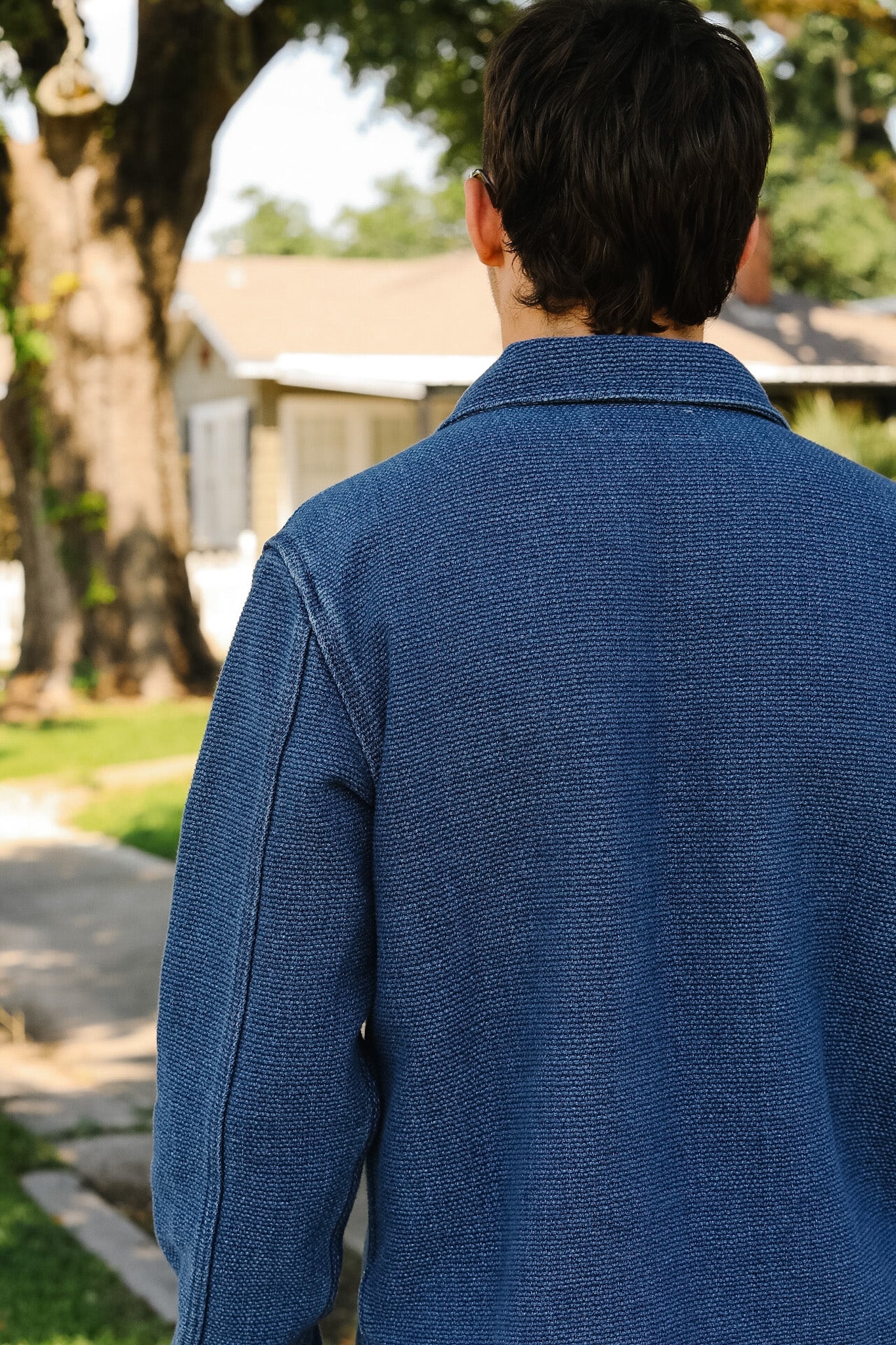 Person wearing a blue textured shirt outdoors with greenery in the background