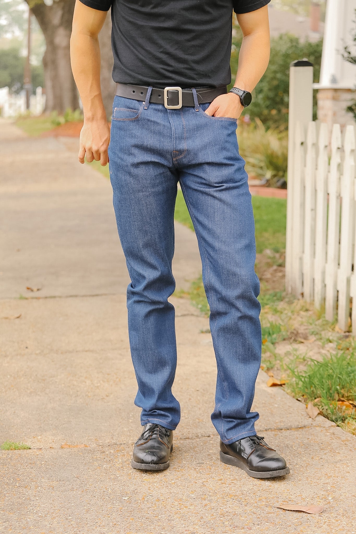 Person wearing blue jeans and black shoes on a sidewalk