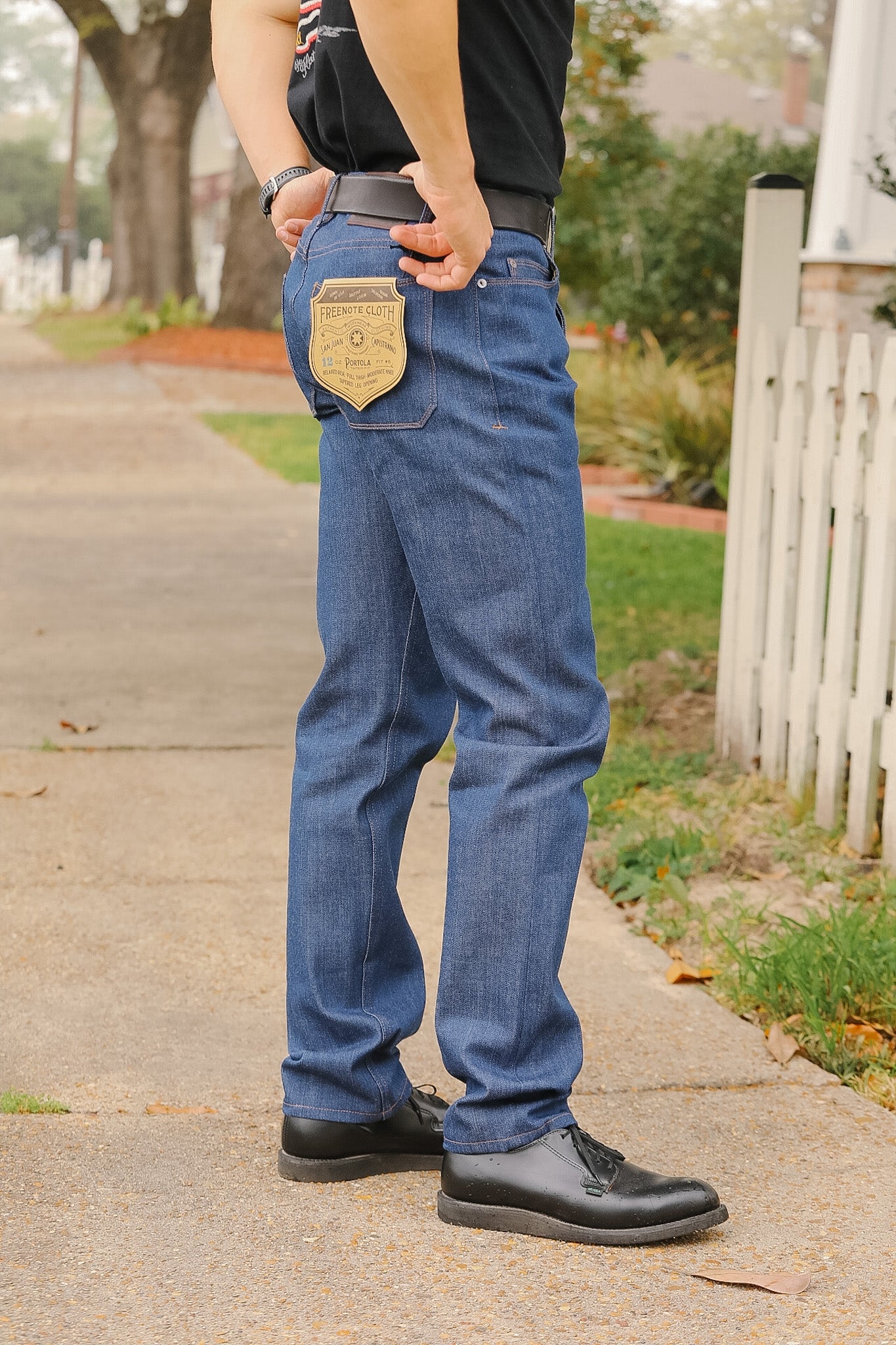 Person wearing blue jeans and black shoes on a sidewalk.