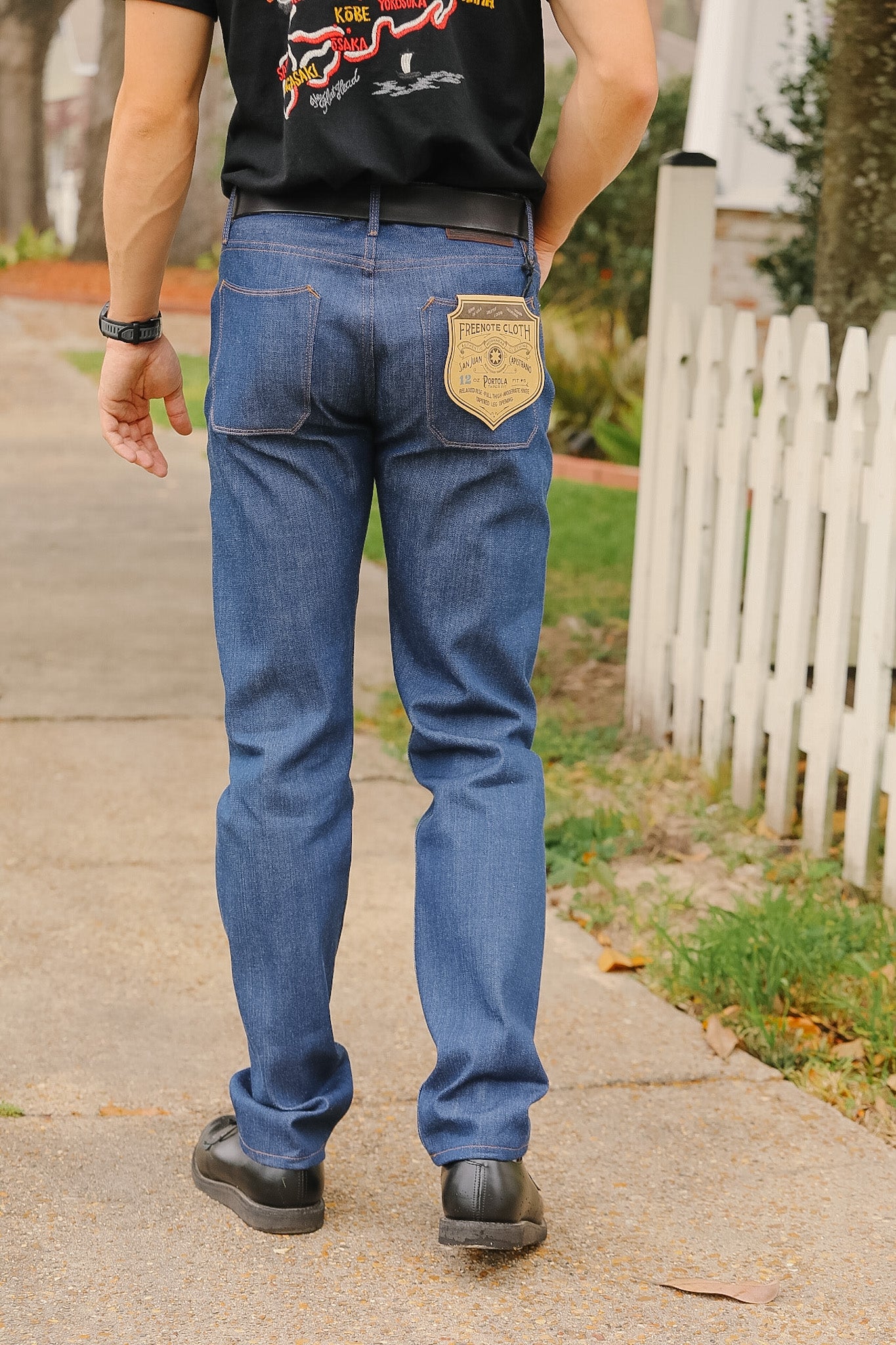 Person wearing blue jeans with a visible brand patch on a sidewalk.