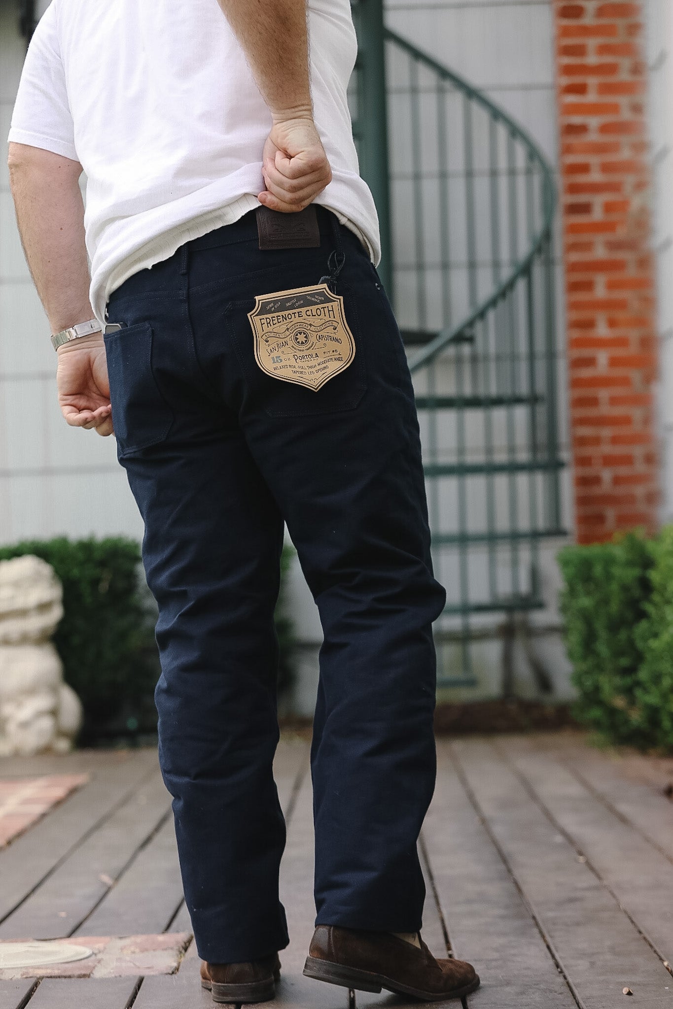 Person wearing navy pants with a decorative patch, standing on a wooden deck.