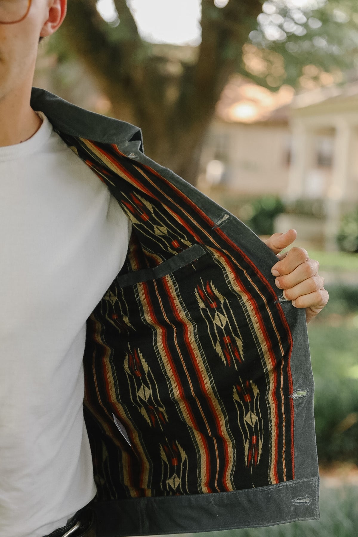 A person outdoors wearing a white t-shirt and holding open a dark gray jacket to show a colorful Southwestern-style striped patterned lining.