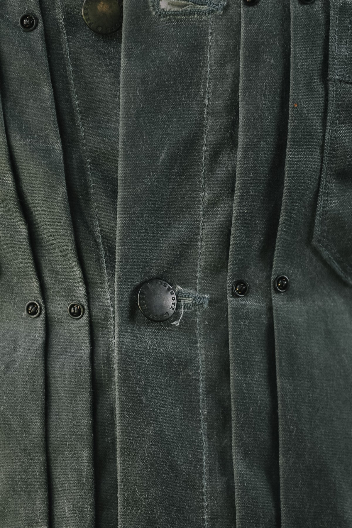 Close-up of a dark gray textured jacket or overshirt with vertical pleats, button closures, and visible fabric wear.
