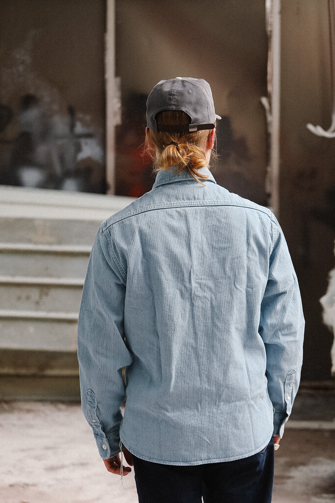 Person wearing a light blue jacket and cap in an indoor setting with blurred background