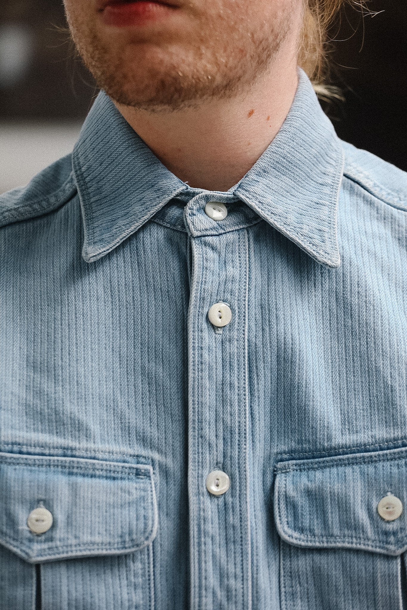 Close-up of a person wearing a light blue denim shirt with a collar.