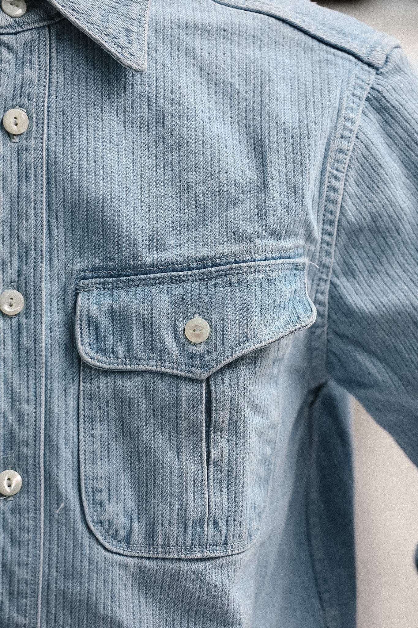 Close-up of a light blue denim shirt with a pocket and buttons.