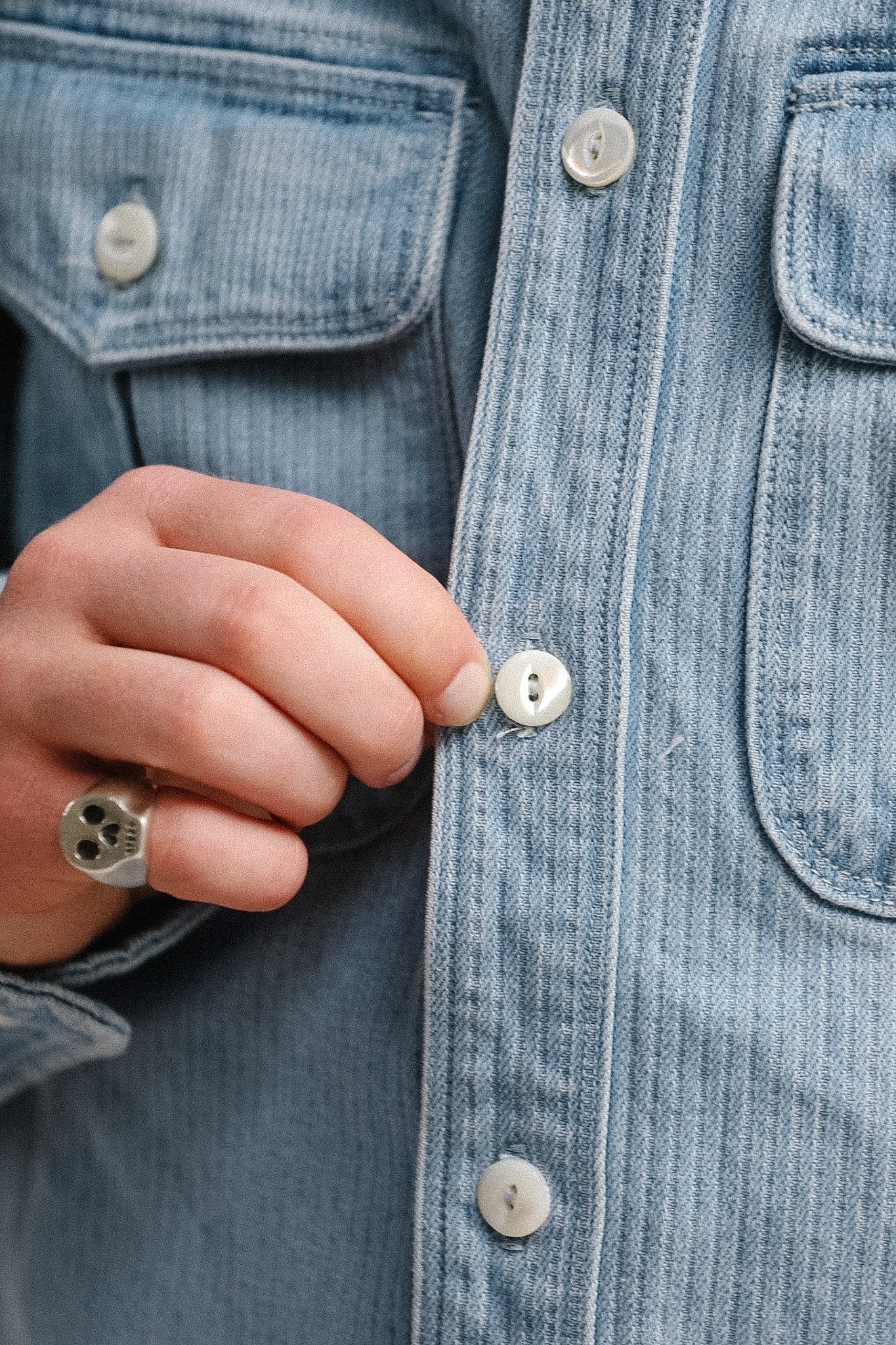 Close-up of a person buttoning a light blue denim jacket.
