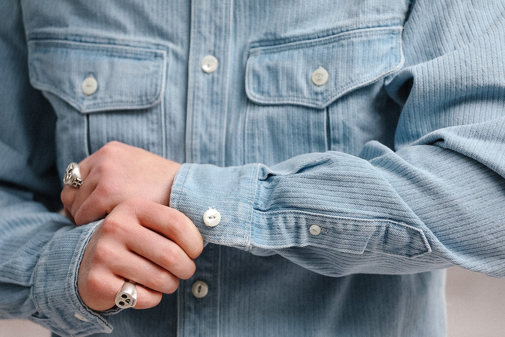 Close-up of a person wearing a light blue denim shirt with rolled-up sleeves.