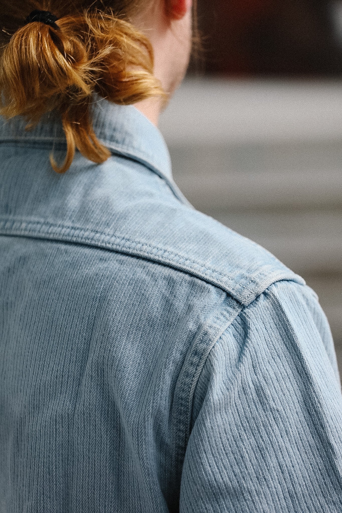 Close-up of a person wearing a light blue denim jacket with blurred background