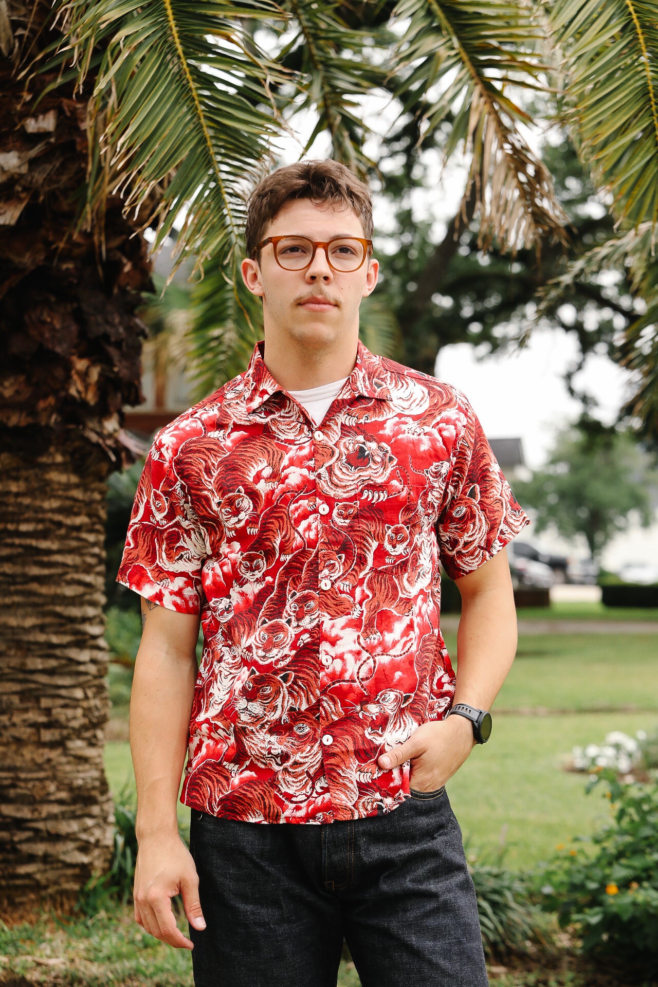 Person wearing a red floral shirt standing outdoors with palm trees in the background