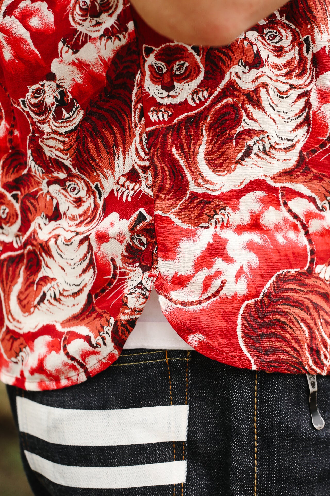 Red and white tiger patterned shirt worn by a person, with denim jeans and a striped shoe visible.