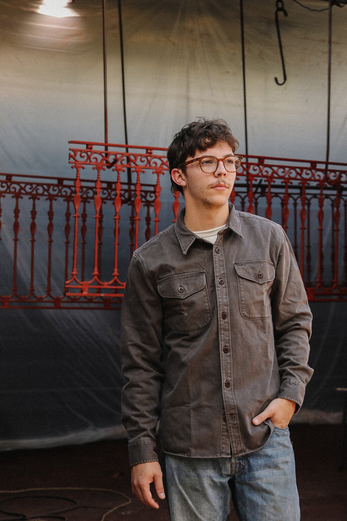 man wearing brown shirt standing in front of metal gate