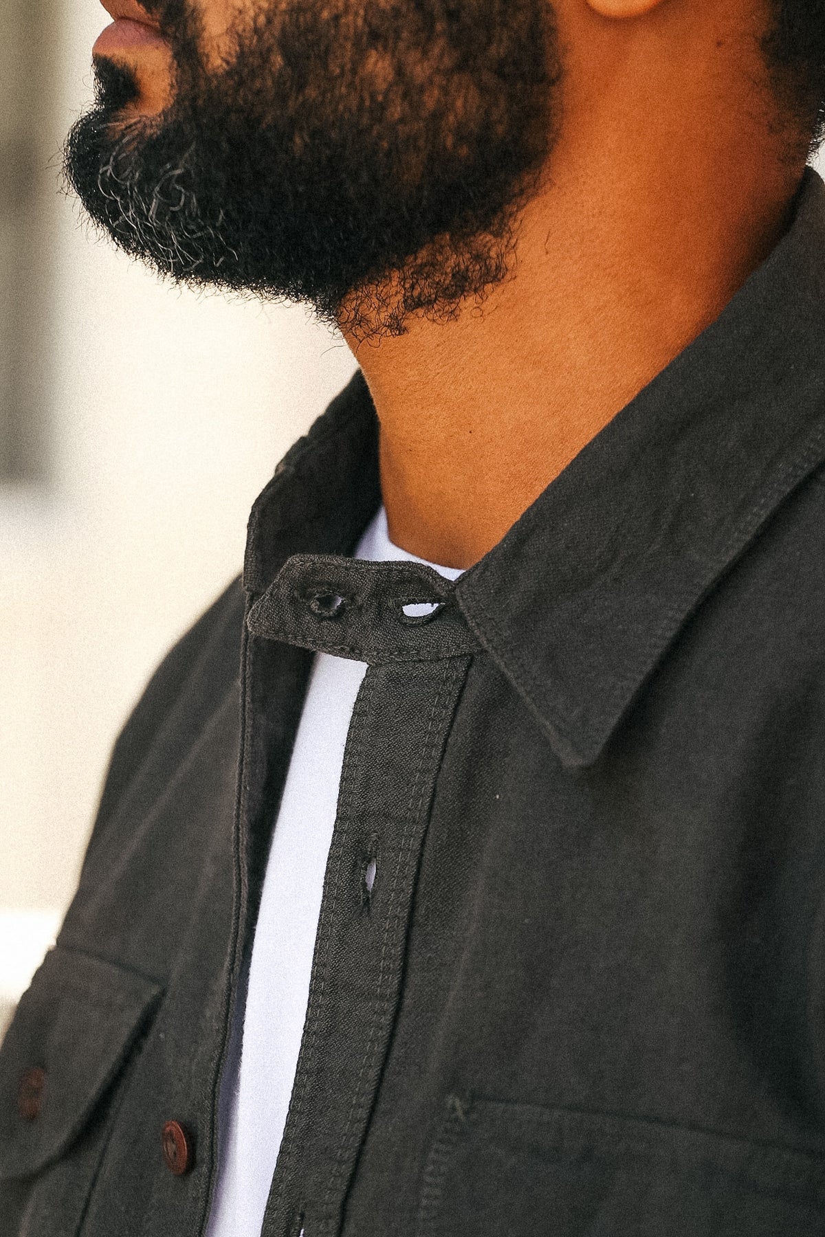 Close-up of a man wearing a dark charcoal gray overshirt over a white t-shirt, showing the collar, button details, and fabric texture.