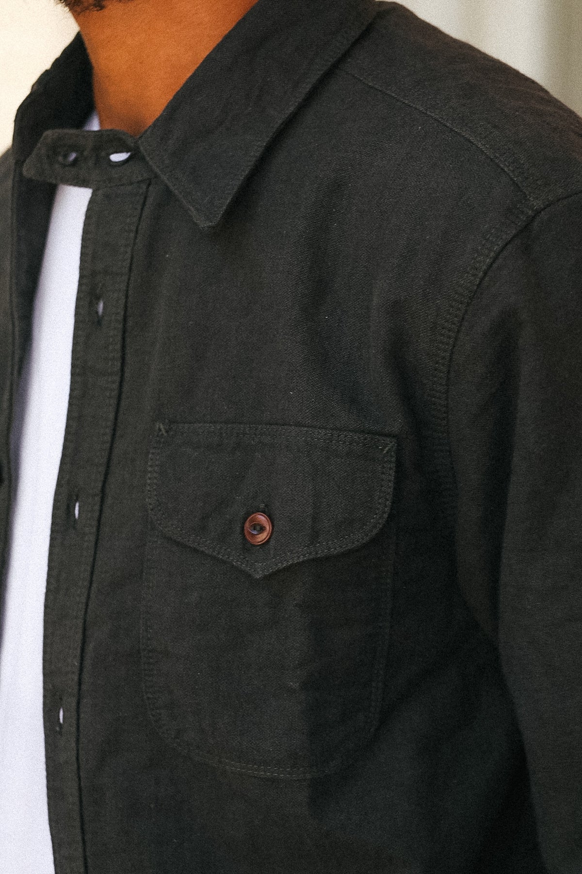 Close-up of a person wearing a dark charcoal gray button-up shirt with a chest pocket and a brown button, layered over a white t-shirt.