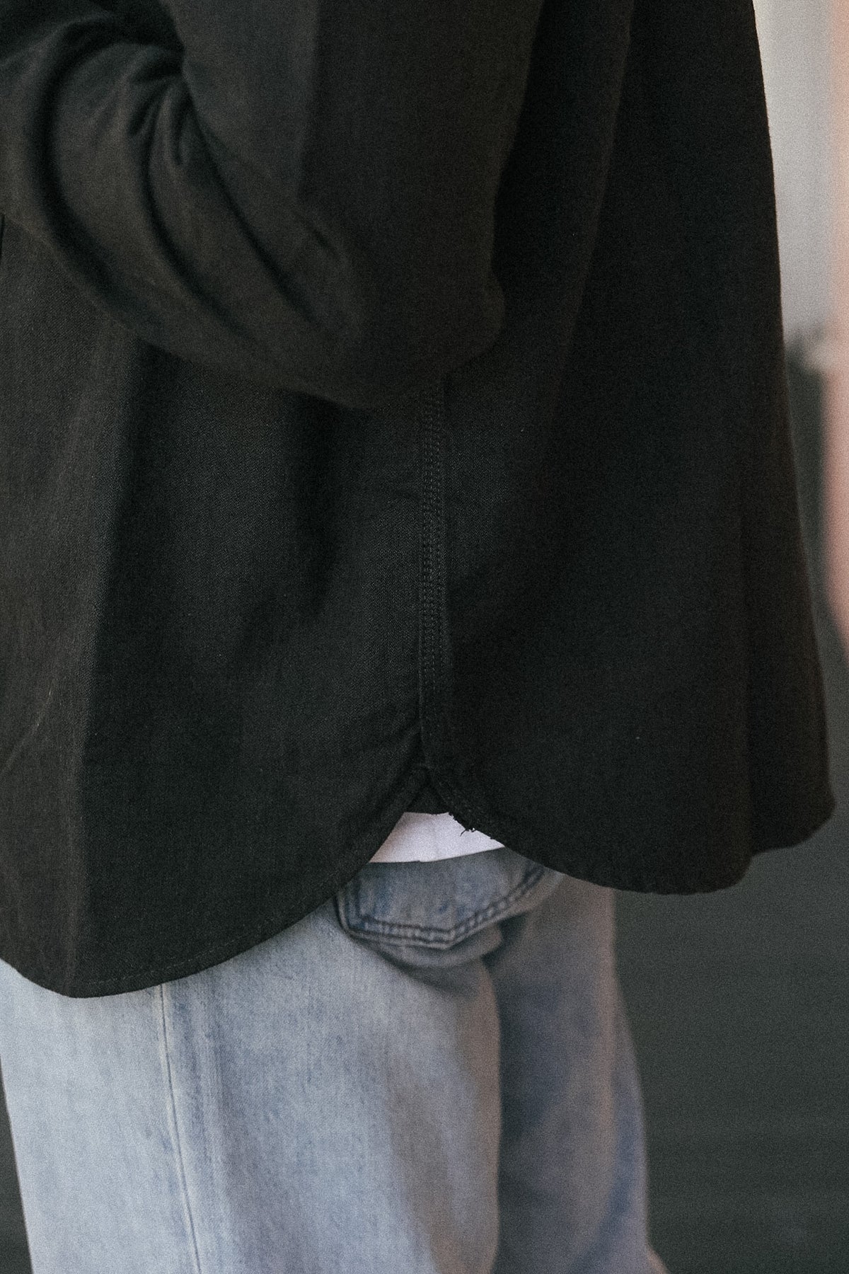 Close-up of a person wearing a black long-sleeve shirt tucked into light blue jeans, showing the side and back drape of the shirt.
